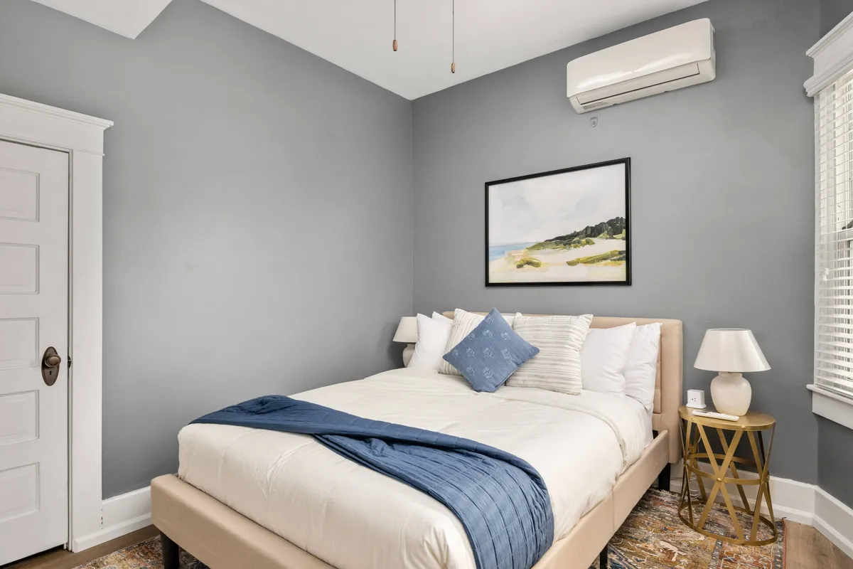 A peaceful bedroom setting with a bed adorned with decorative pillows, a calm painting above, and a soft bedside lamp. The mood is tranquil and restful, ideal for relaxation after a productive day or for unwinding during quiet hours.