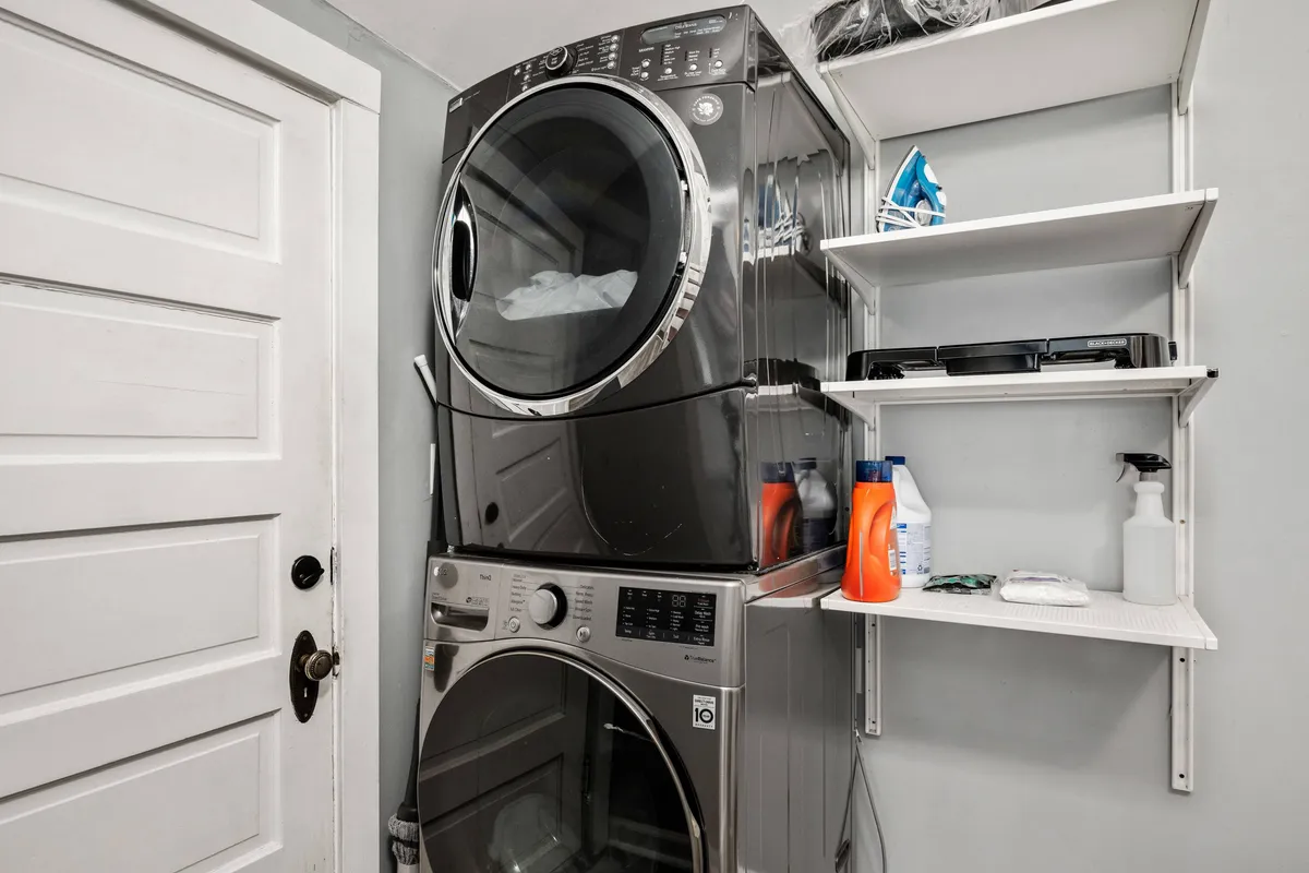 This image features a stacked washer and dryer unit positioned near a door that seemingly leads to the exterior, with shelves holding laundry supplies. The presence of the door provides an implicit connection to the outside, suggesting convenience for cleaning up after outdoor adventures with pets.