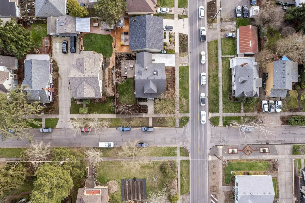 A peaceful residential street lined with mature trees, featuring charming houses and well-maintained gardens. The scene hints at a welcoming, walkable neighborhood ideal for leisurely strolls to nearby destinations.
