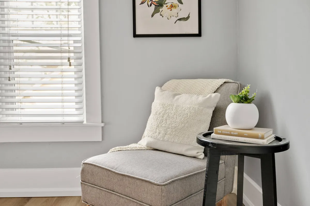 A cozy reading nook featuring a comfortable chair adorned with a decorative pillow, a small side table for coffee or a laptop, framed artwork, and a vibrant plant. Natural light bathes the corner, creating an inviting space for focused work or contemplation.