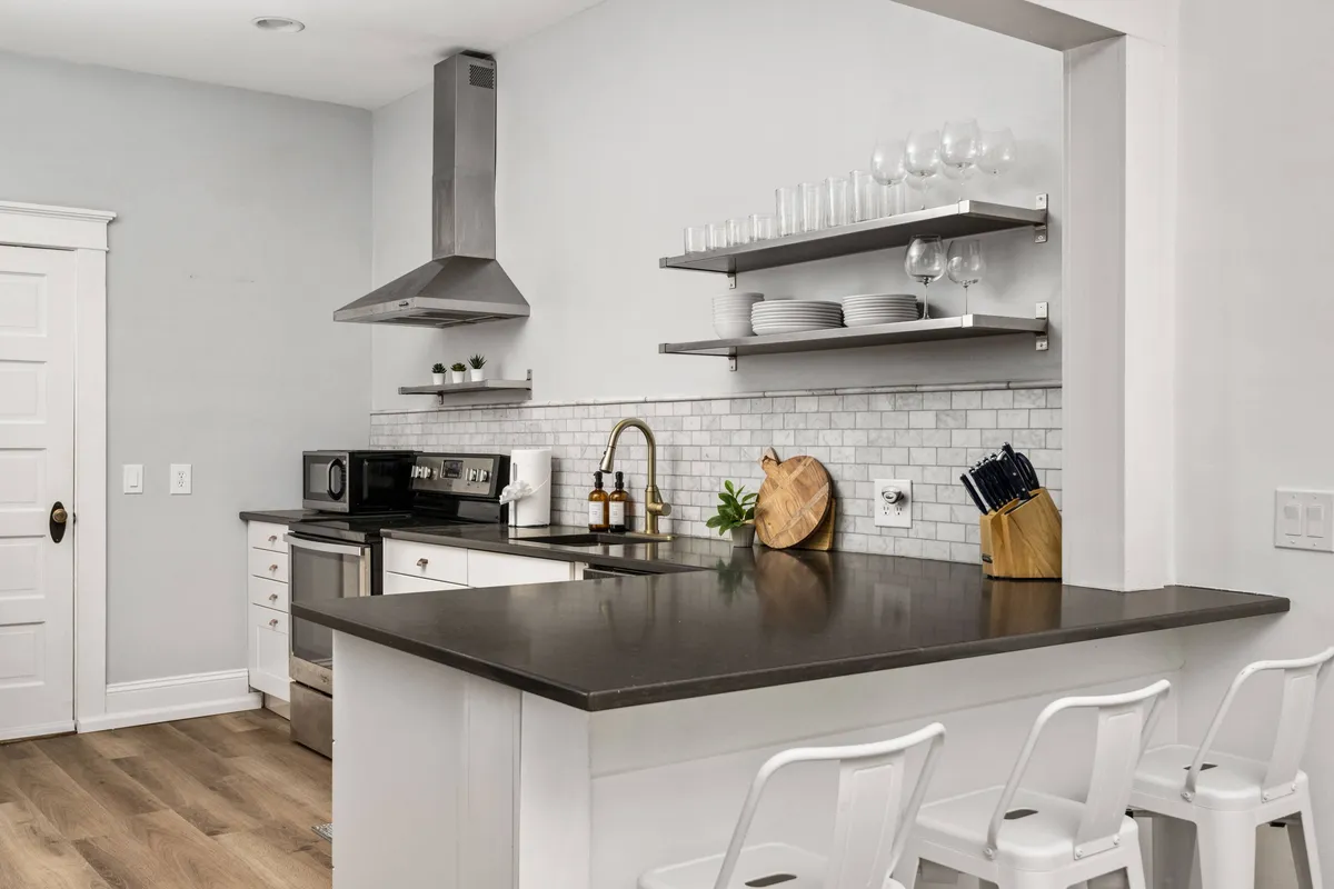 A functional, well-appointed kitchen with a central island, ample countertop space, modern appliances, and open shelving displaying dishes. The space exudes practicality as well as warmth, inviting culinary pursuits and group activities.